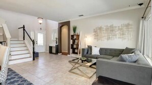 A spacious living room with a grey sofa, a coffee table, and a staircase leading to another area. - Luxurious spa-like oasis with pool, 4bdr/ 3br (Elk Grove)