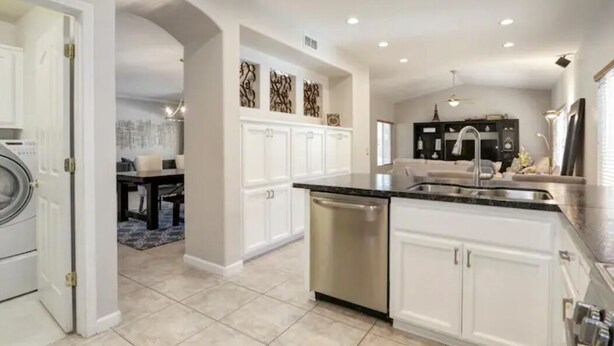 A modern kitchen with white cabinets, a stainless steel dishwasher, and a black countertop. - Luxurious spa-like oasis with pool, 4bdr/ 3br (Elk Grove)