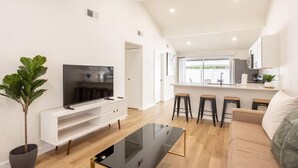 Un salon moderne avec un téléviseur à écran plat, une table basse et un canapé. Il y a également un coin cuisine avec un bar et des tabourets.
