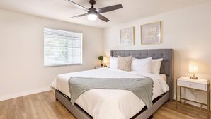 Une chambre à coucher comprenant un lit, une table de chevet, un ventilateur de plafond et deux tableaux encadrés accrochés au mur.
