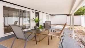 Une terrasse extérieure avec une porte vitrée donnant sur une pièce, une table avec des chaises et une plante en pot.