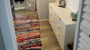 En smal gang med et mønstret tæppe, et hvidt skab med skuffer, en lille plante og et vægmonteret ur.