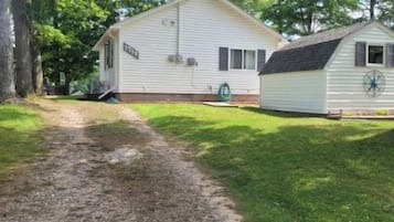 A single-story mobile home with a gravel driveway, surrounded by trees.