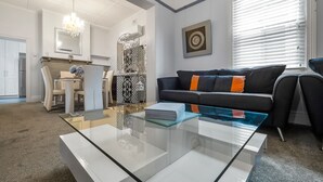 A modern living room with a glass coffee table, a sofa with orange cushions, and a dining area in the background. - The Cottage - Lithgow (Lithgow)