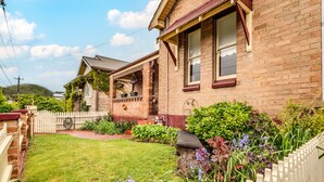 A two-story brick house with a well-maintained garden, a white picket fence, and a clear sky. - The Cottage - Lithgow (Lithgow)