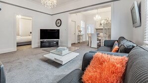 A spacious living room with a flat-screen TV, a glass coffee table, and a modern sofa with orange pillows. - The Cottage - Lithgow (Lithgow)