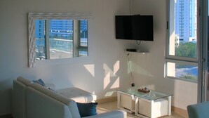 Un salon moderne avec un canapé blanc, une table basse en verre et un téléviseur à écran plat fixé au mur.