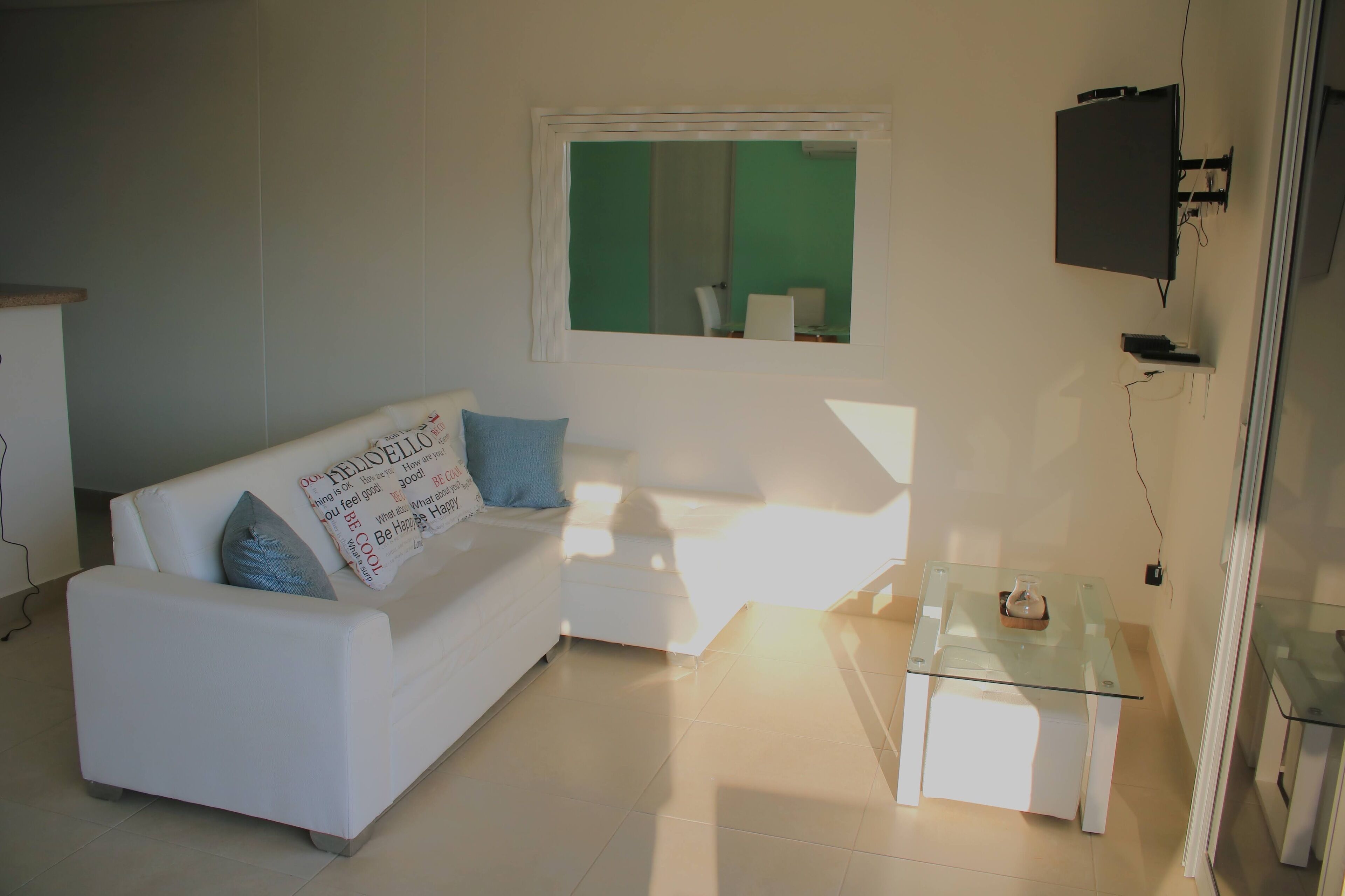 A modern living room with a white sofa, a glass coffee table, and a television mounted on the wall.