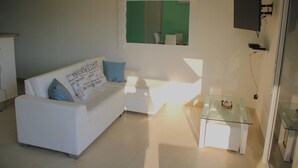 Un salon moderne avec un canapé blanc, une table basse en verre et un téléviseur fixé au mur.