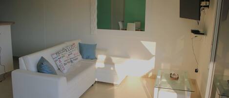 A modern living room with a white sofa, a glass coffee table, and a television mounted on the wall.