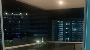 Un balcon doté de meubles en osier et offrant une vue sur la ville la nuit.