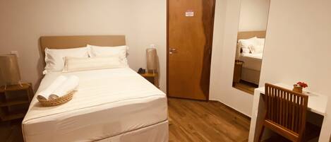 A neatly arranged bedroom with a bed, bedside tables, a desk, and a chair.