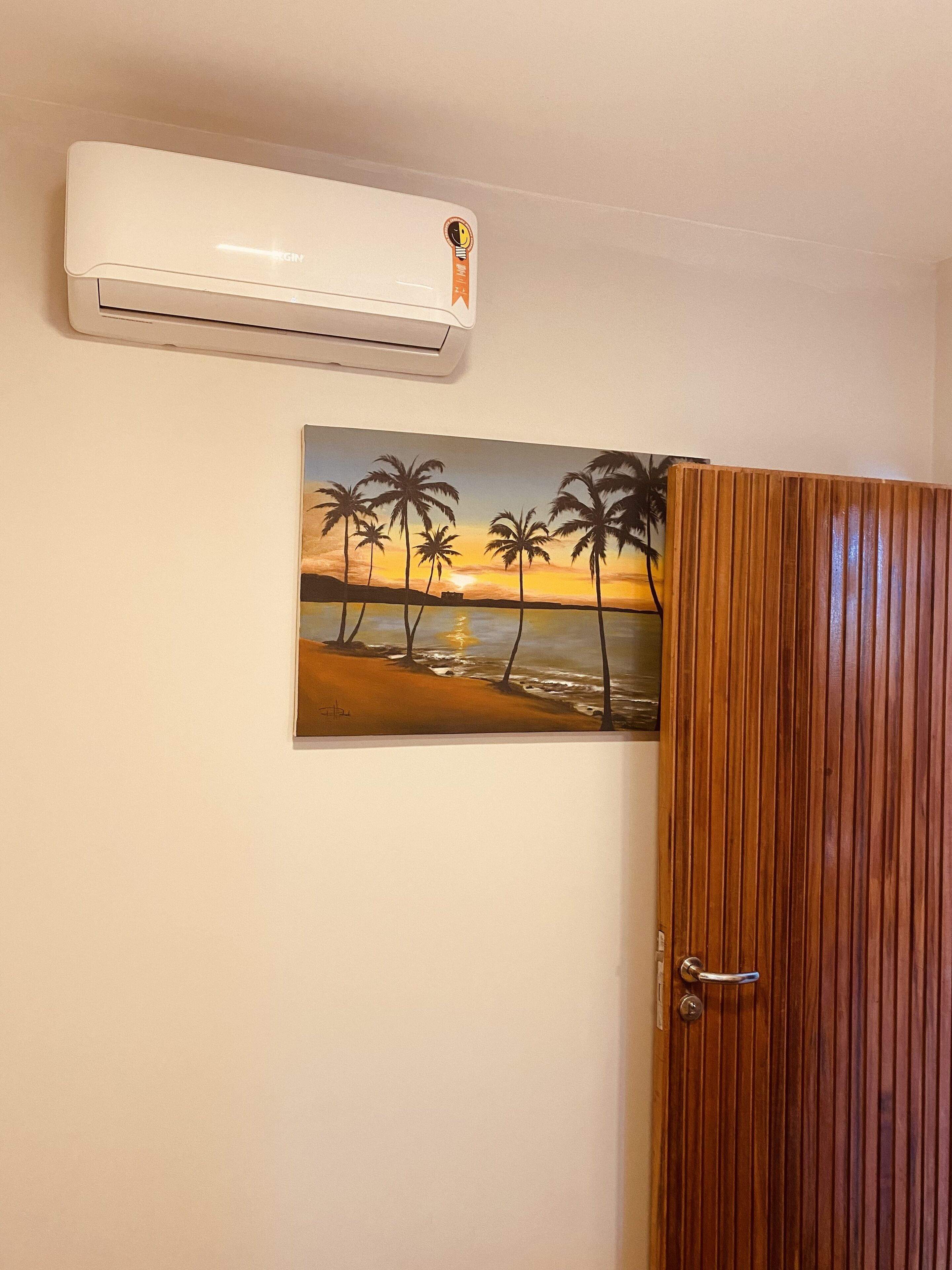 Een kamer met een houten deur, een wandairconditioner en een schilderij van een strand.