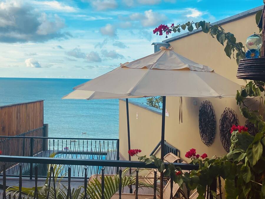 Un balcone con vista sul mare, un ombrellone bianco e mobili in vimini.