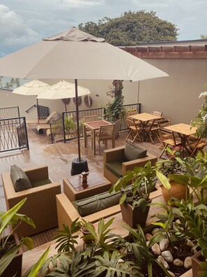 Een terras buiten met wicker meubels, parasols en potplanten.