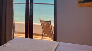 A room with a bed, a chair, and a view of the ocean through a sliding door. - Beach Eco Stays Hotel Boutique Lagoinha (Paraipaba)