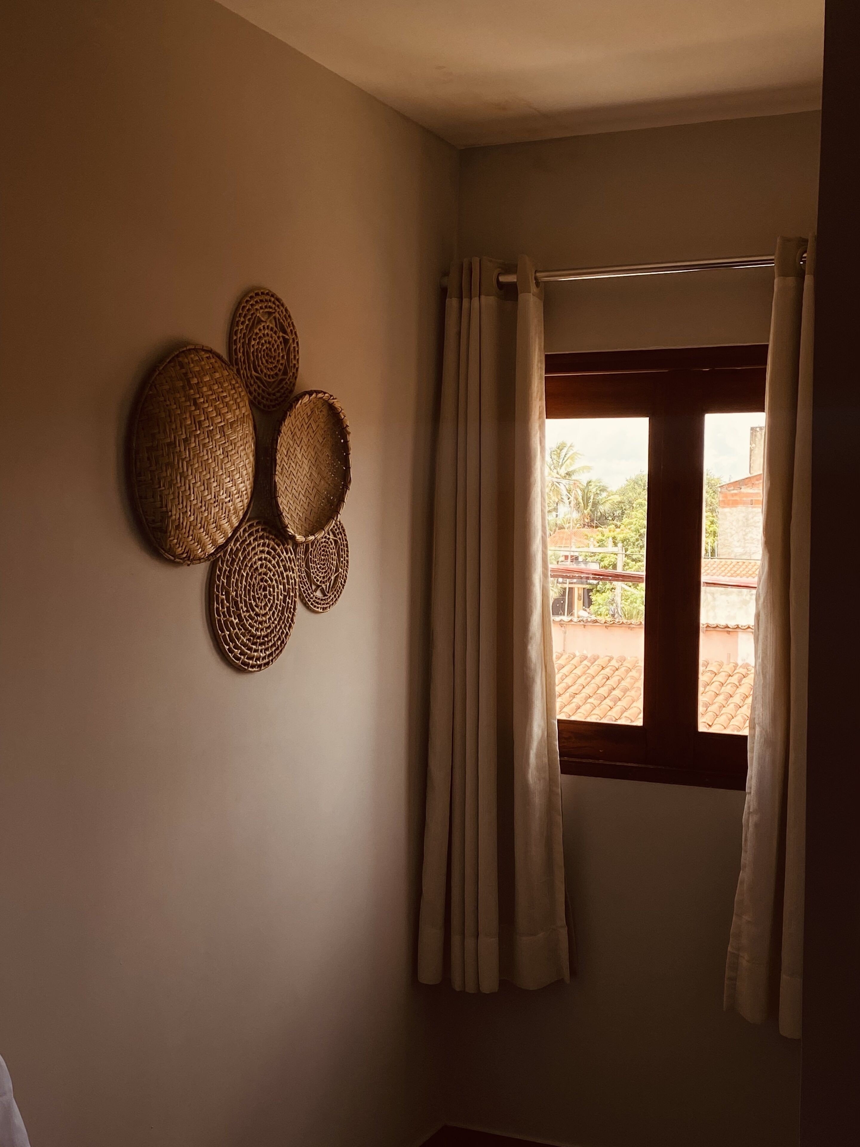A room with a window, curtains, and woven wall decorations.