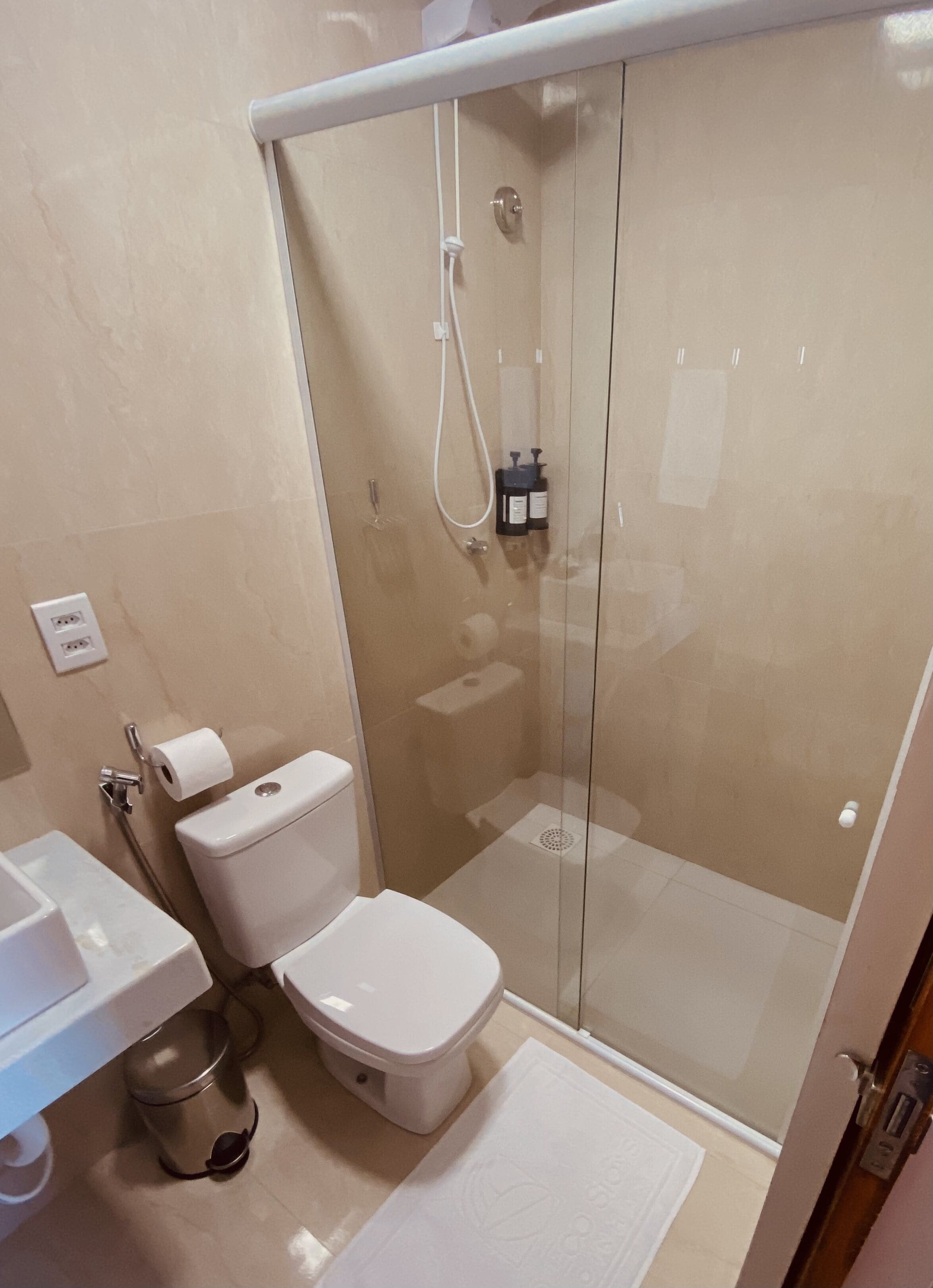 A modern bathroom with a glass-enclosed shower, a toilet, a sink, and a trash bin.