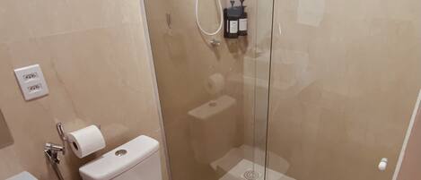 A modern bathroom with a glass-enclosed shower, a toilet, a sink, and a trash bin.