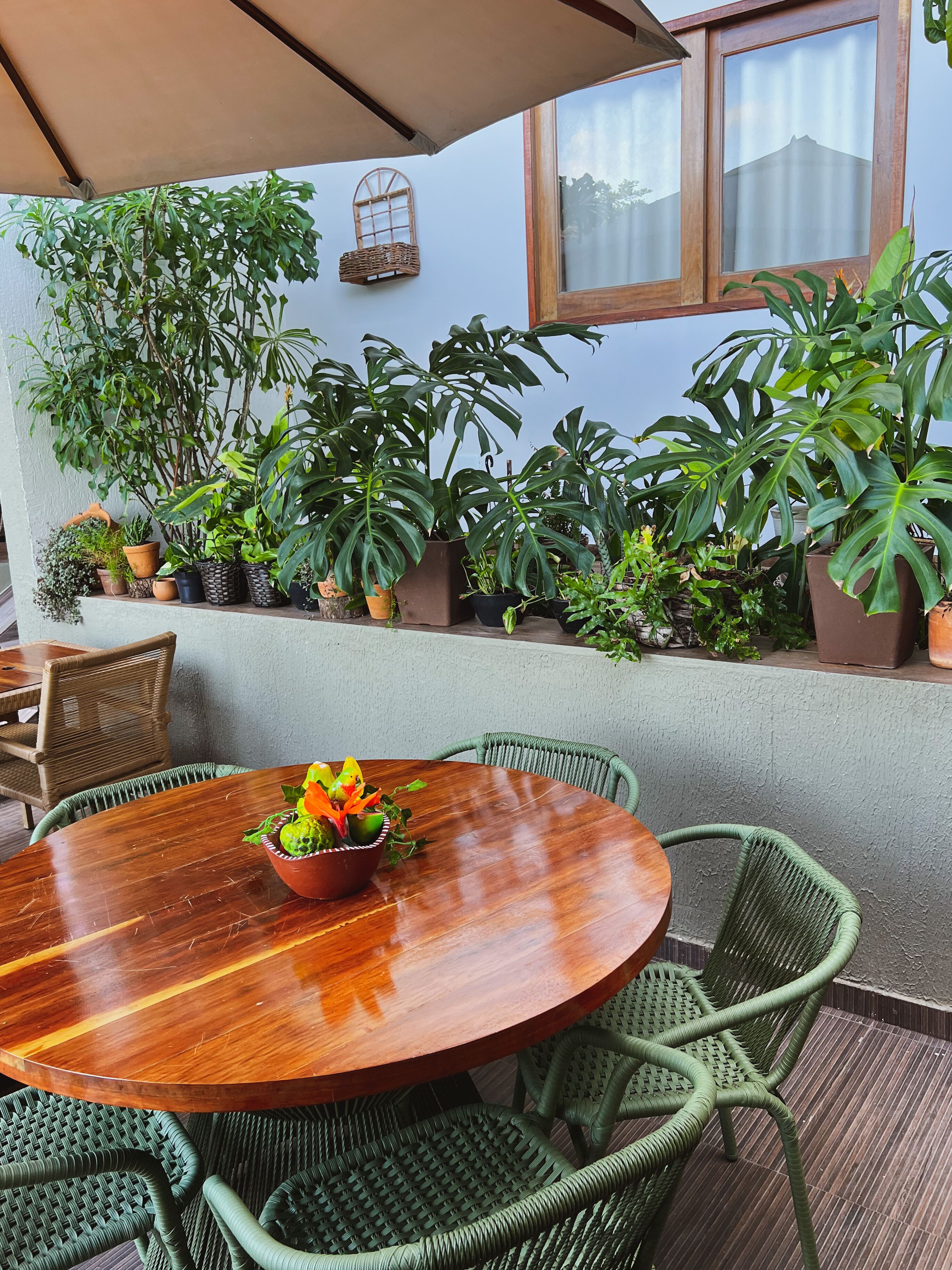 Una mesa redonda de madera con sillas, rodeada de plantas en macetas y una silla de mimbre.