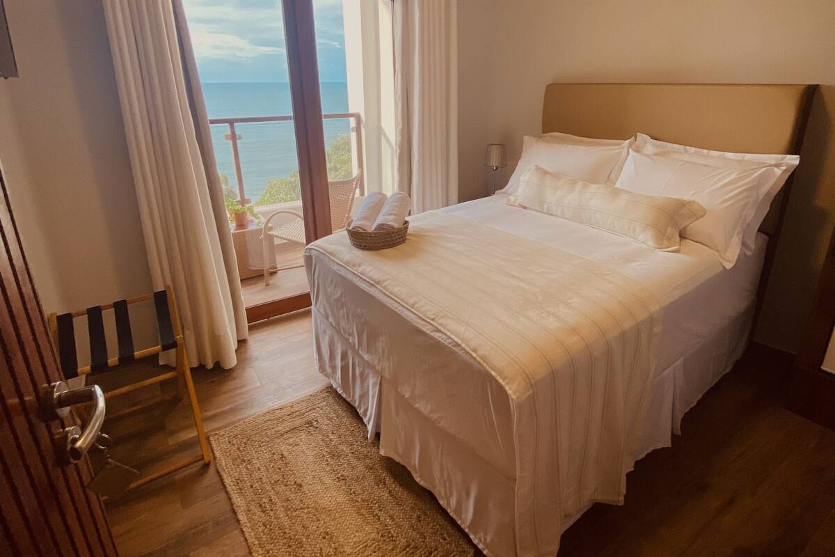 A bedroom with a bed, a view of the sea, and a balcony.