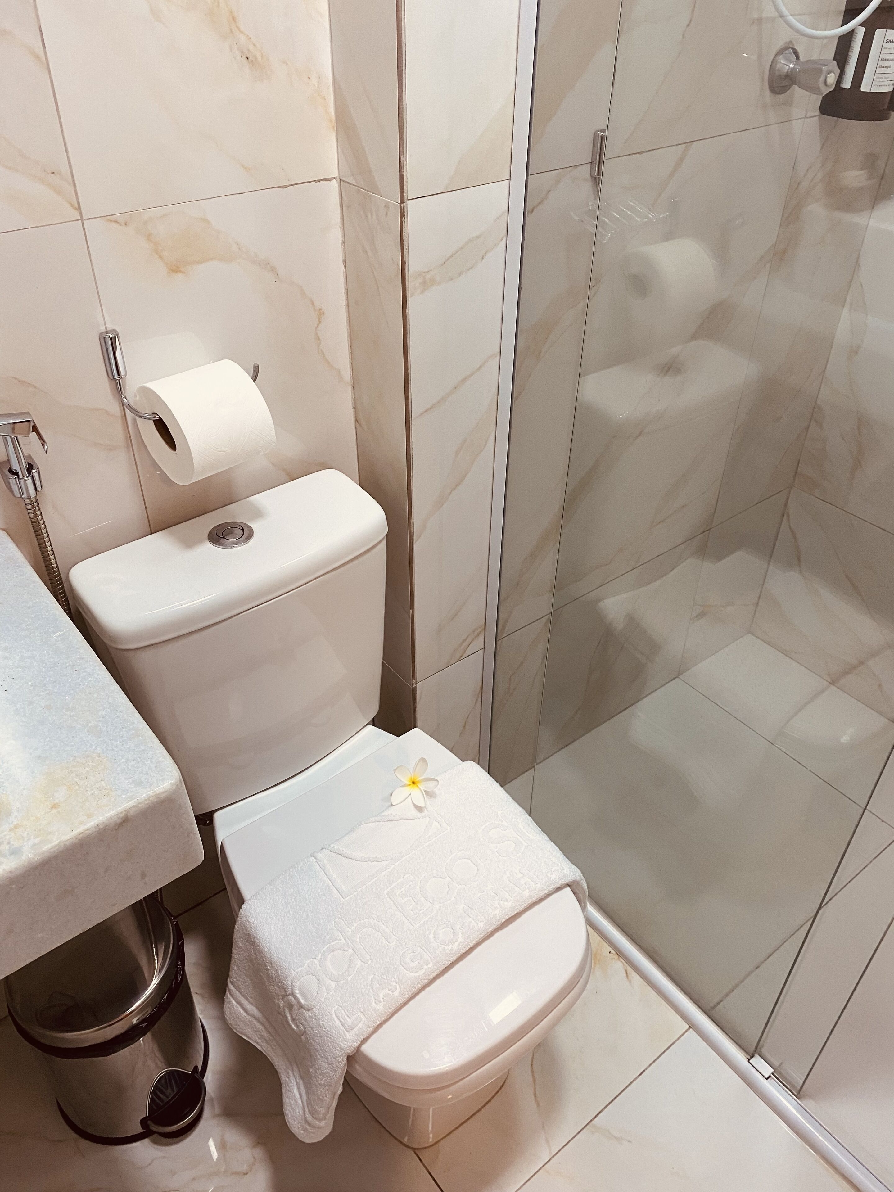 A bathroom with a toilet, a shower, and a trash bin.