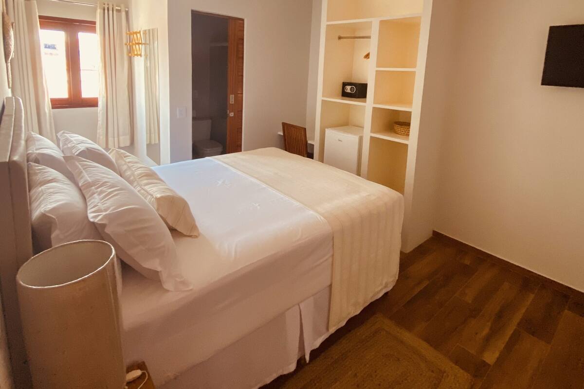 A hotel room with a bed, a desk, a chair, a TV, and a wardrobe.
