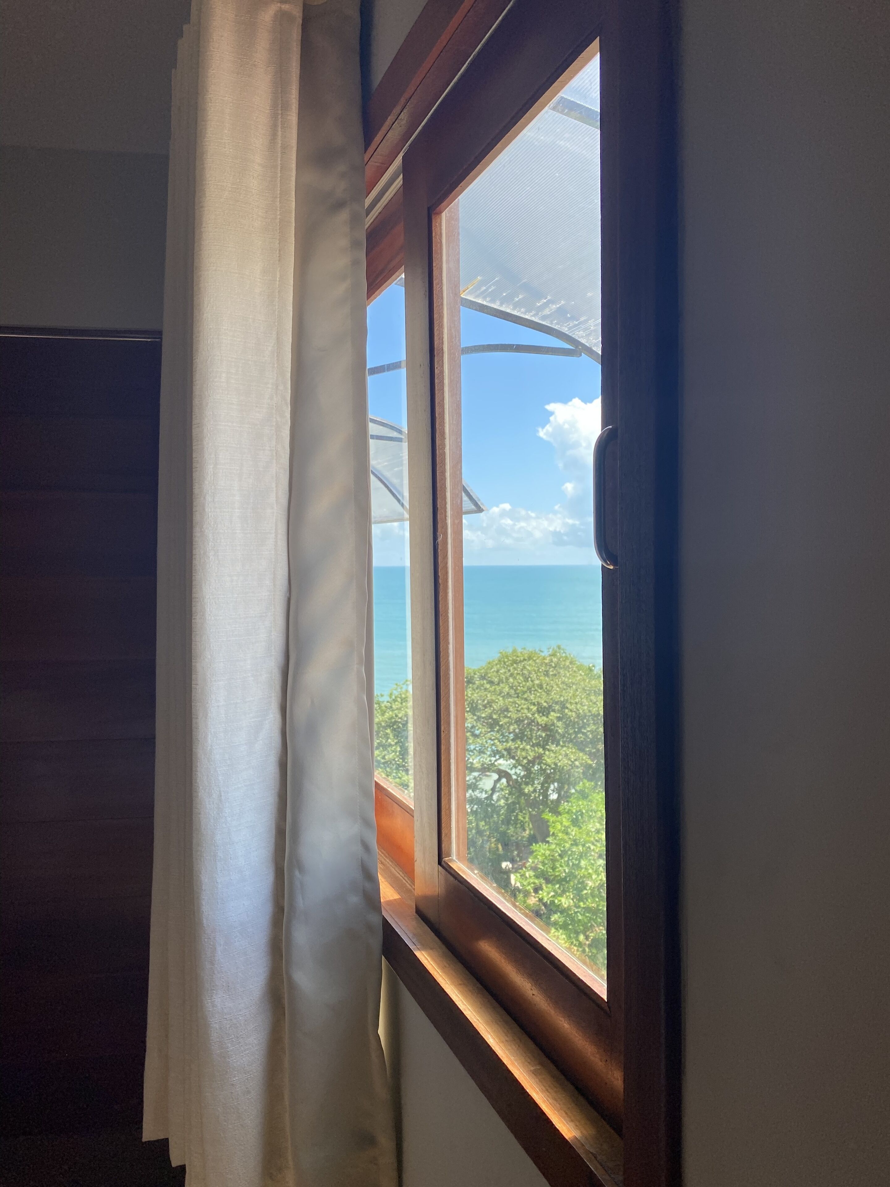 Une fenêtre donnant sur un paysage tropical et l’océan.