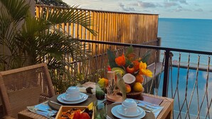 A dining table set with plates, glasses, and a fruit bowl on a balcony with a view of the sea. - Beach Eco Stays Hotel Boutique Lagoinha (Paraipaba)