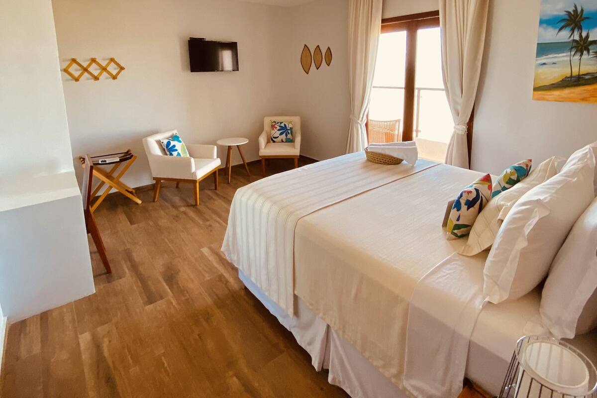 A bedroom with a bed, a desk, a chair, a TV, and a painting on the wall.