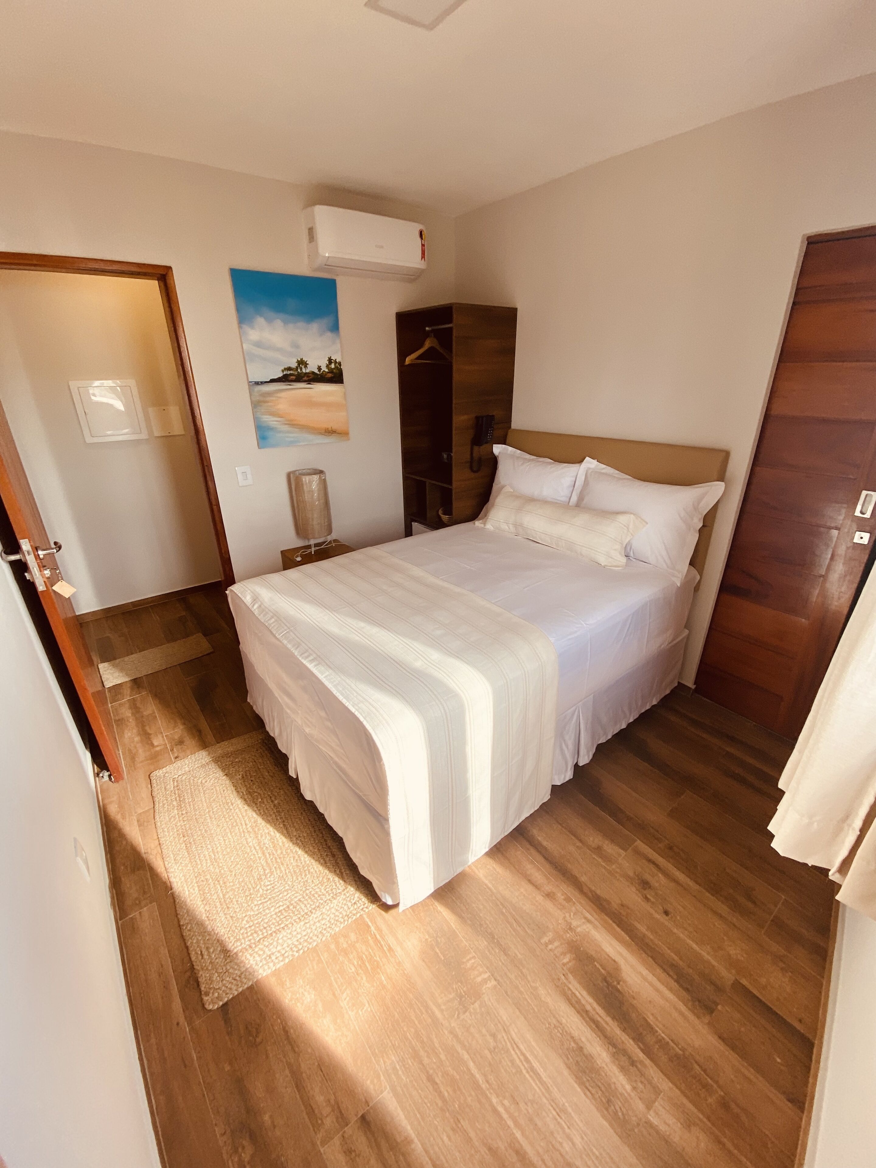 Ein Schlafzimmer mit einem großen Bett, einem Holzschrank, einem Gemälde an der Wand und einer Deckenklimaanlage.