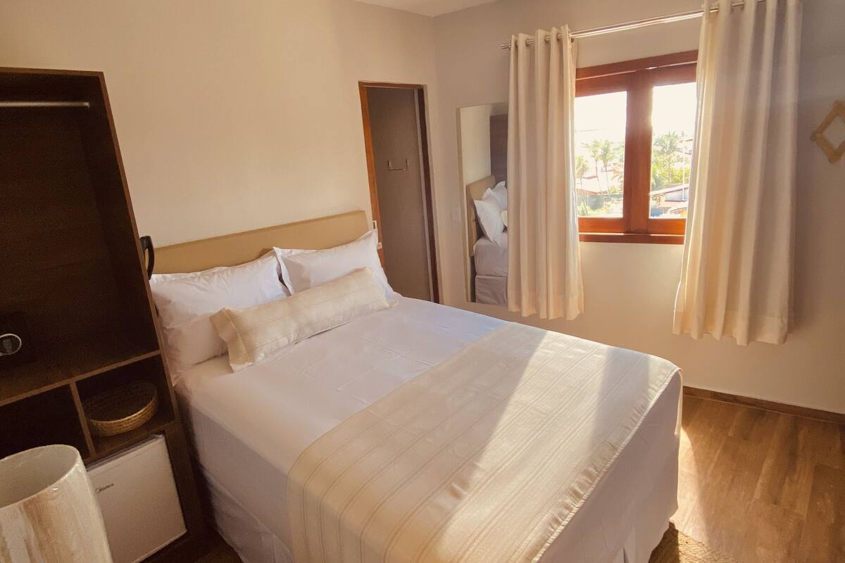 A hotel room with a bed, a TV, a bedside table, a lamp, and a window with curtains.