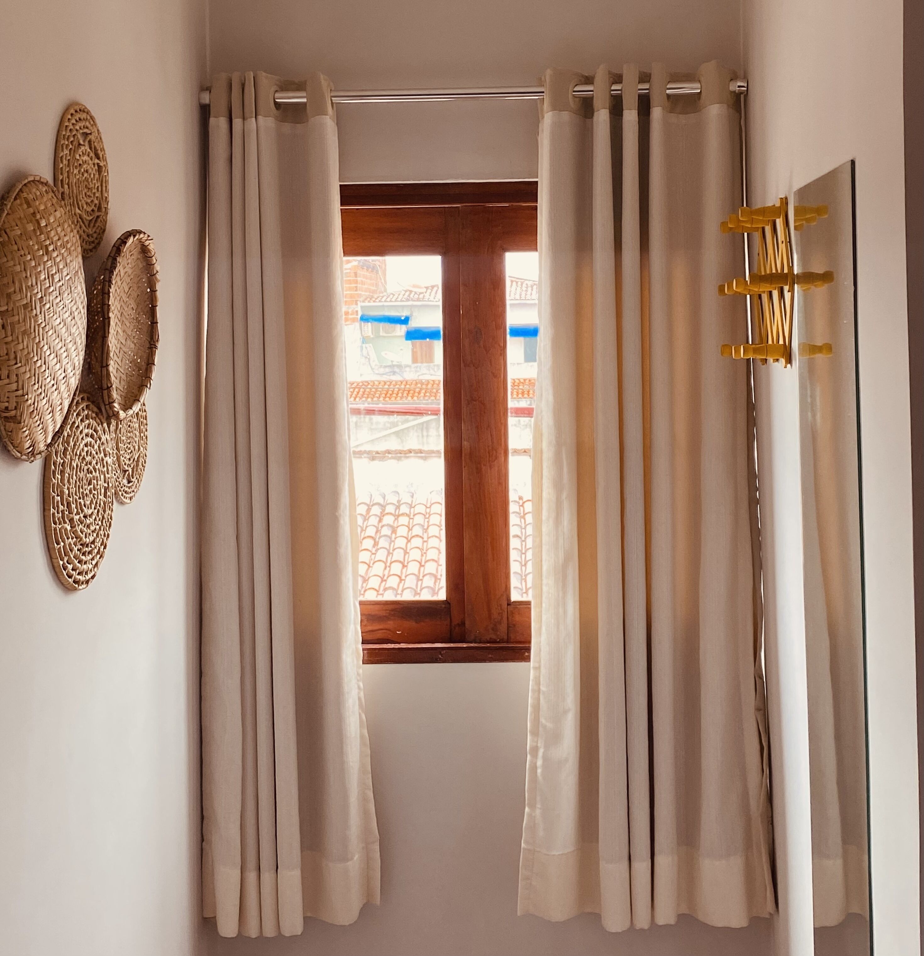 Una habitación con ventana, cortinas blancas y adornos de pared tejidos.