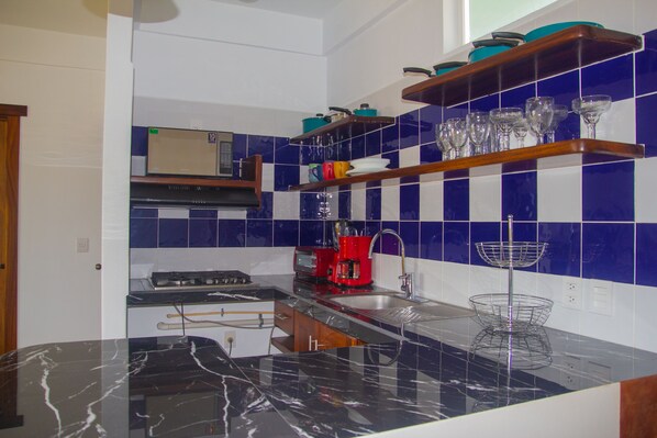 A kitchen with a black marble countertop, a red coffee maker, and blue and white tiled backsplash. - Hotel Happy Beach (Zihuatanejo)