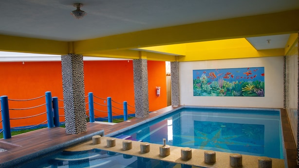 An indoor swimming pool with a tiled deck, surrounded by a yellow and orange wall with a mural. - Hotel Happy Beach (Zihuatanejo)