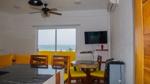 A dining area with a large table, yellow chairs, a ceiling fan, and a TV mounted on the wall. - Hotel Happy Beach (Zihuatanejo)