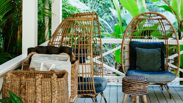 Un porche cubierto con mobiliario de mimbre, luces cálidas y exuberante follaje tropical.