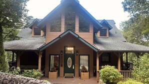 A two-story house with a steeply pitched roof, a front porch with a stone wall, and a green door. - 3 level cabin on Mt Mitchell golf course (Burnsville)