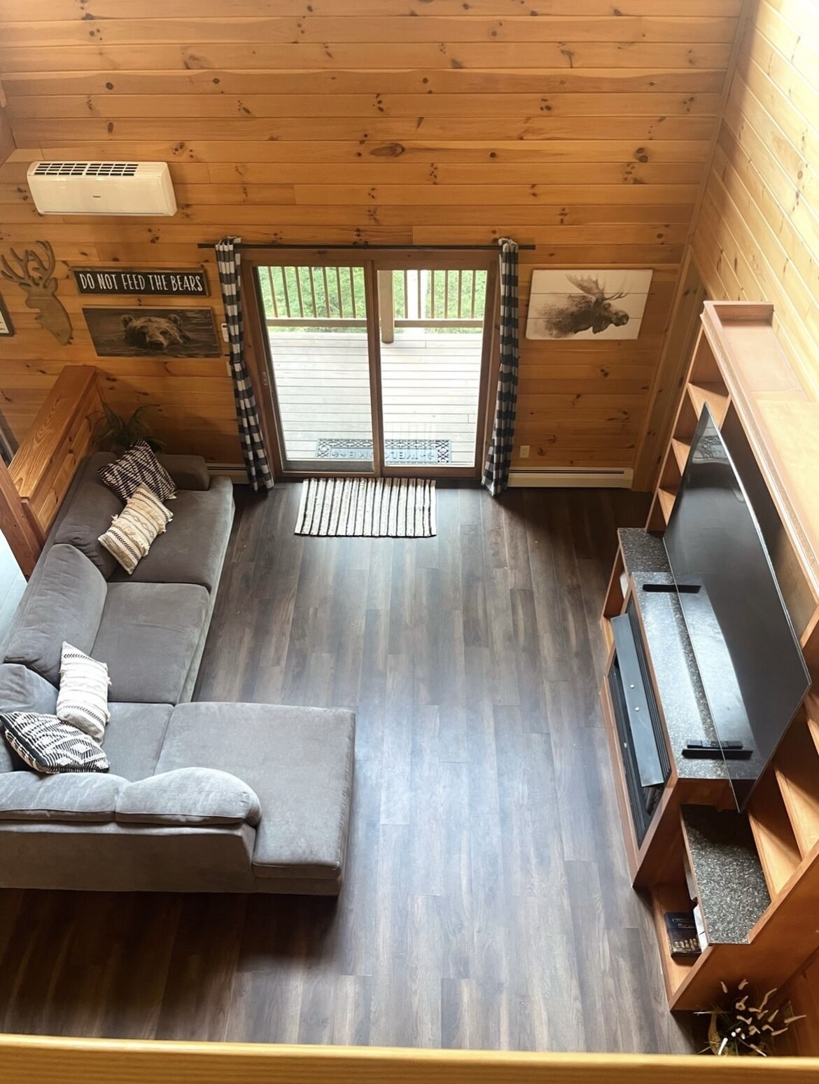 Un interior de cabaña acogedor, con un sofá gris, un televisor de pantalla plana y techo de madera.