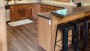 A kitchen with wooden cabinets, a granite countertop, and a bar area with stools. - 3 level cabin on Mt Mitchell golf course (Burnsville)