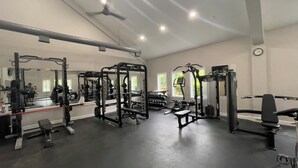 Un gimnasio con diversos equipos de ejercicio, espejos y un reloj en la pared.