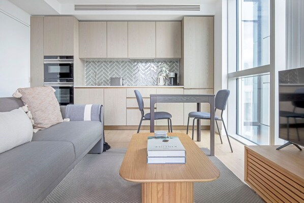 A modern living room with a grey sofa, a wooden coffee table, and a dining area with a table and chairs.