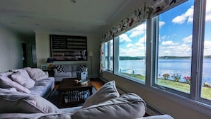 Ein Wohnzimmer mit großem Fenster mit Seeblick, einer Couch, einem Couchtisch und einer Flagge an der Wand.
