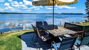 Eine Terrasse im Freien mit Tisch und Stühlen, einem Sonnenschirm und Blick auf einen See.