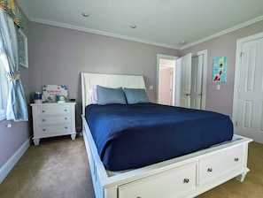 Un dormitorio con cama blanca, mesita de noche, cómoda y una puerta.