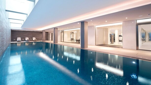 A modern indoor swimming pool with clear water, lounge chairs, and glass-walled changing rooms. - Trendy South Bank 1BR w/ Pool, Gym & Concierge, nr Tube, by Blueground (London)