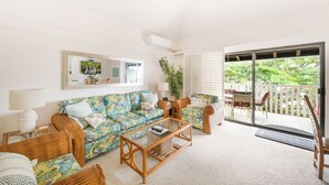 Ein Wohnzimmer mit einer Couch, Sesseln, einem Couchtisch und einer Schiebetür, die auf einen Balkon führt.