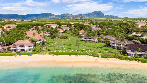 Ein Resort mit Strandvillen, einer zentralen Rasenfläche und Blick auf den Ozean und die Berge.