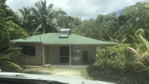 A single-story building with a green roof, surrounded by dense tropical vegetation. - Two bedroom house - spacious, clean and comfortable in great location. (Niue)