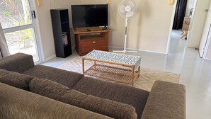 A living room with a sofa, a television, a stand fan, and a small table. - Two bedroom house - spacious, clean and comfortable in great location. (Niue)